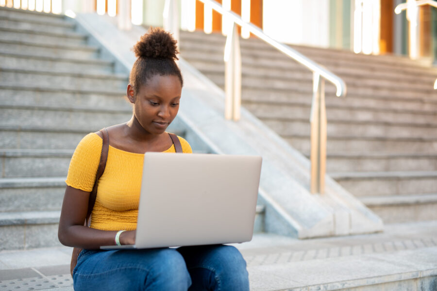 young african american student sitting with her laptop on her knees, working and studying online content, modern technology and internet connection lifestyle